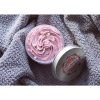 Otevřená růžová sprchová šlehačka Rose Oud s nadýchanou texturou položená na šedé pletené dece